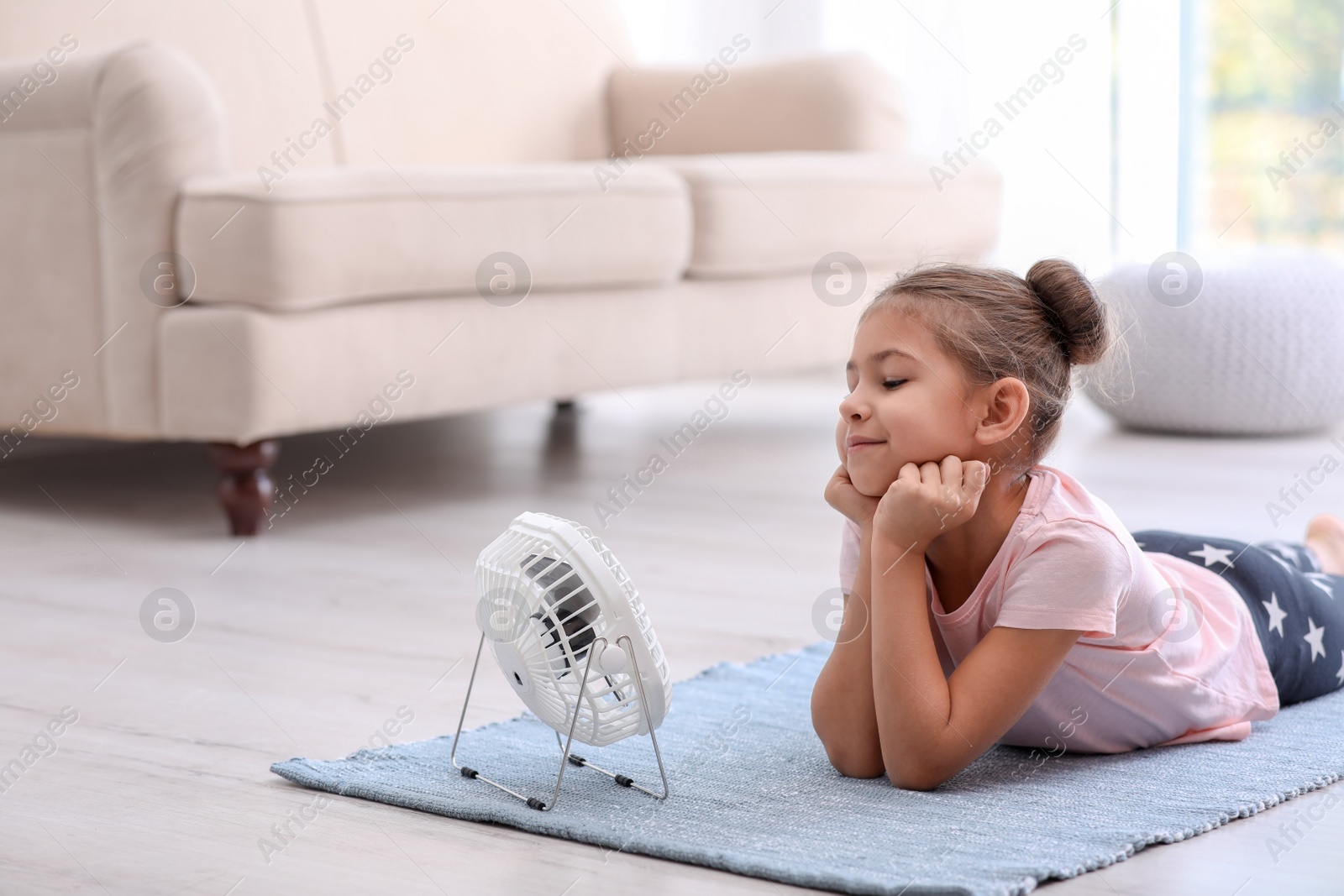 Photo of Little girl relaxing in front of fan at home. Summer heat