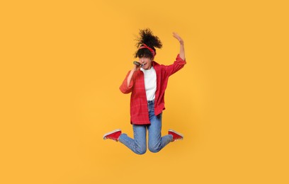 Photo of Beautiful young woman with microphone singing and jumping on yellow background