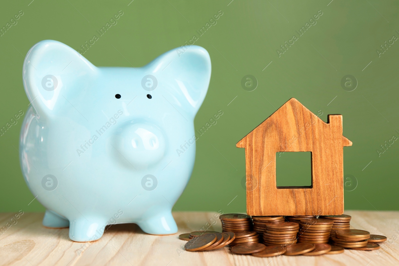 Photo of House model, coins and piggy bank on wooden table against green background