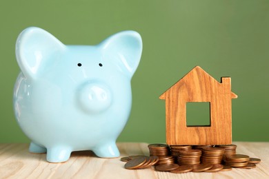 Photo of House model, coins and piggy bank on wooden table against green background