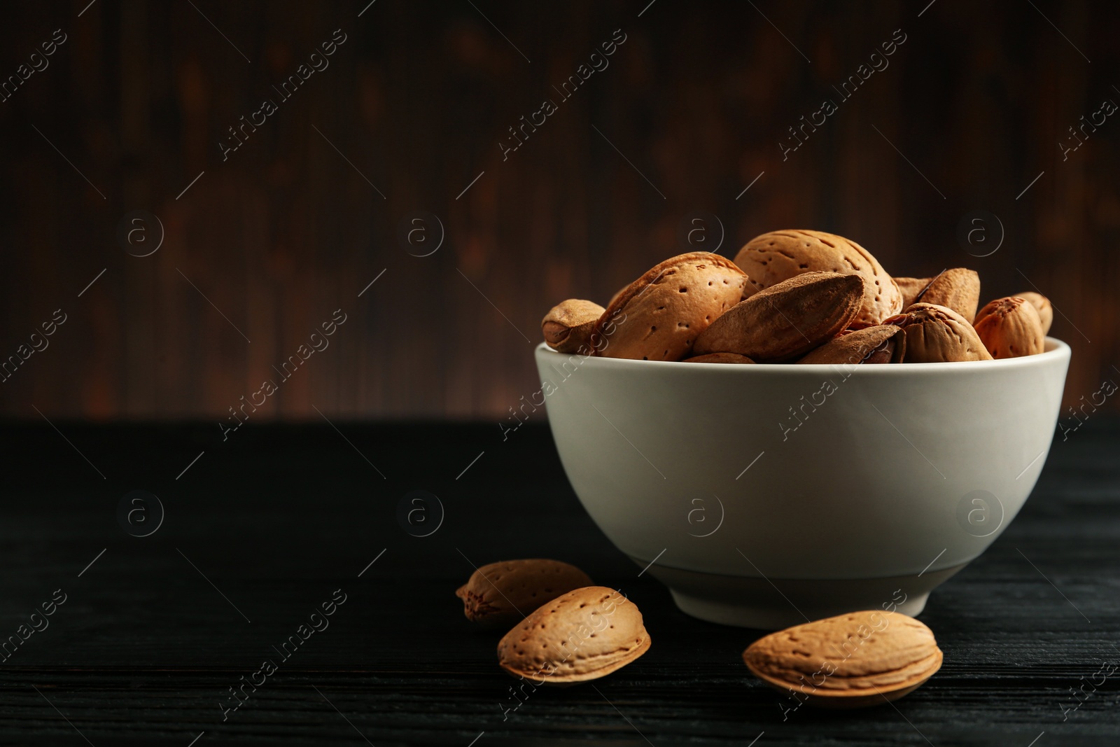 Photo of Ceramic bowl with almonds on black wooden table, space for text. Cooking utensil