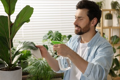 Photo of Man spraying beautiful potted houseplants with water indoors