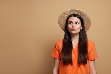 Photo of Beautiful young woman in straw hat giving kiss on beige background. Space for text