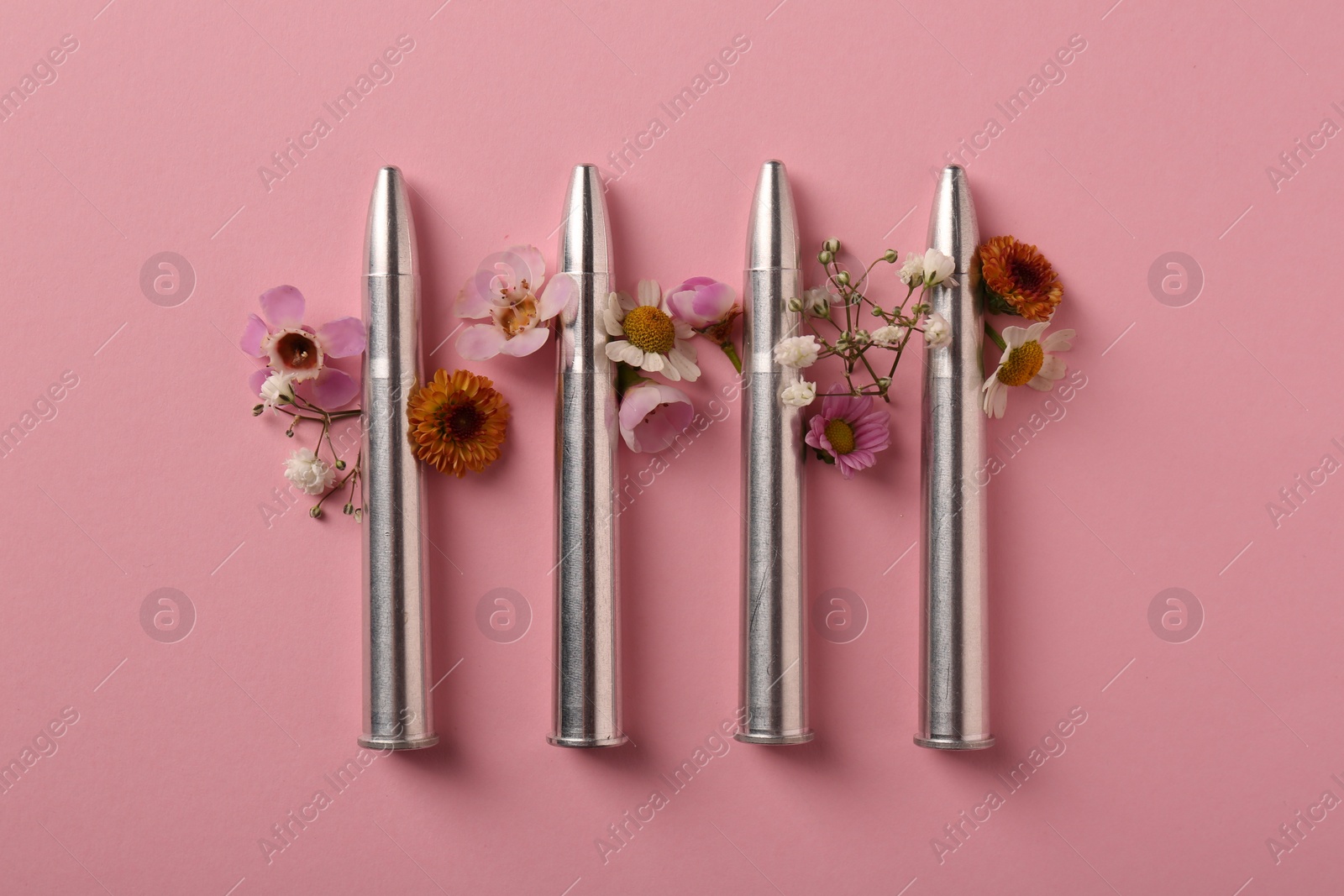 Photo of Metal bullets and beautiful flowers on pink background, flat lay