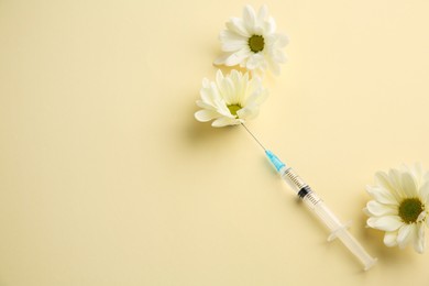 Photo of Medical syringe and beautiful chrysanthemum flowers on pale yellow background, above view. Space for text