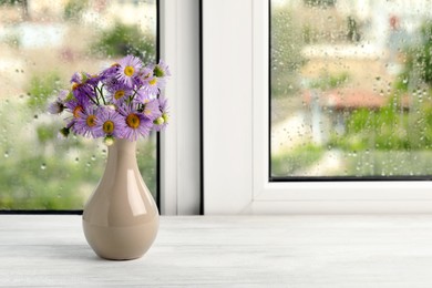 Photo of Vase with flowers near window on rainy day. Space for text