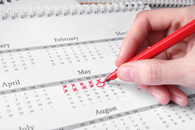 Woman marking date in calendar with red felt pen, closeup