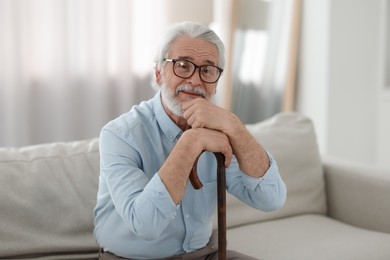 Portrait of grandpa with glasses and walking cane on sofa indoors