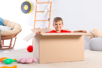 Photo of Cute little boy playing with cardboard box at home