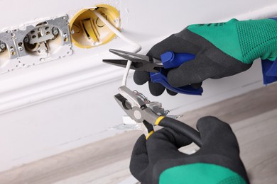 Photo of Professional repairman fixing power sockets with pliers indoors, closeup