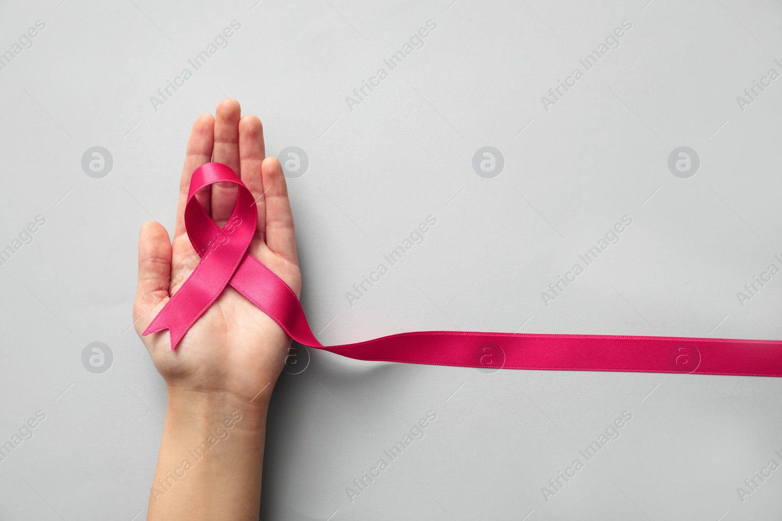 Photo of Woman holding pink ribbon on light grey background, top view. Breast cancer awareness concept