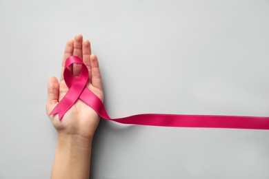 Woman holding pink ribbon on light grey background, top view. Breast cancer awareness concept