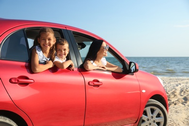 Photo of Happy woman and her children in car near sea. Summer trip