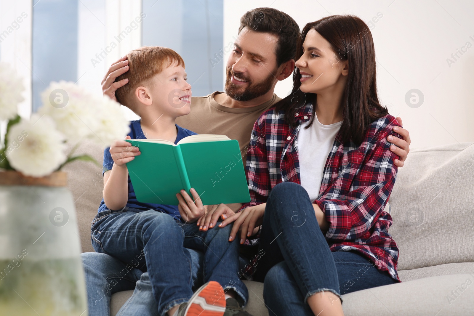 Photo of Happy parents with their child reading book on couch at home