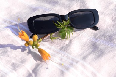 Photo of Stylish sunglasses and tropical flower on blanket, closeup