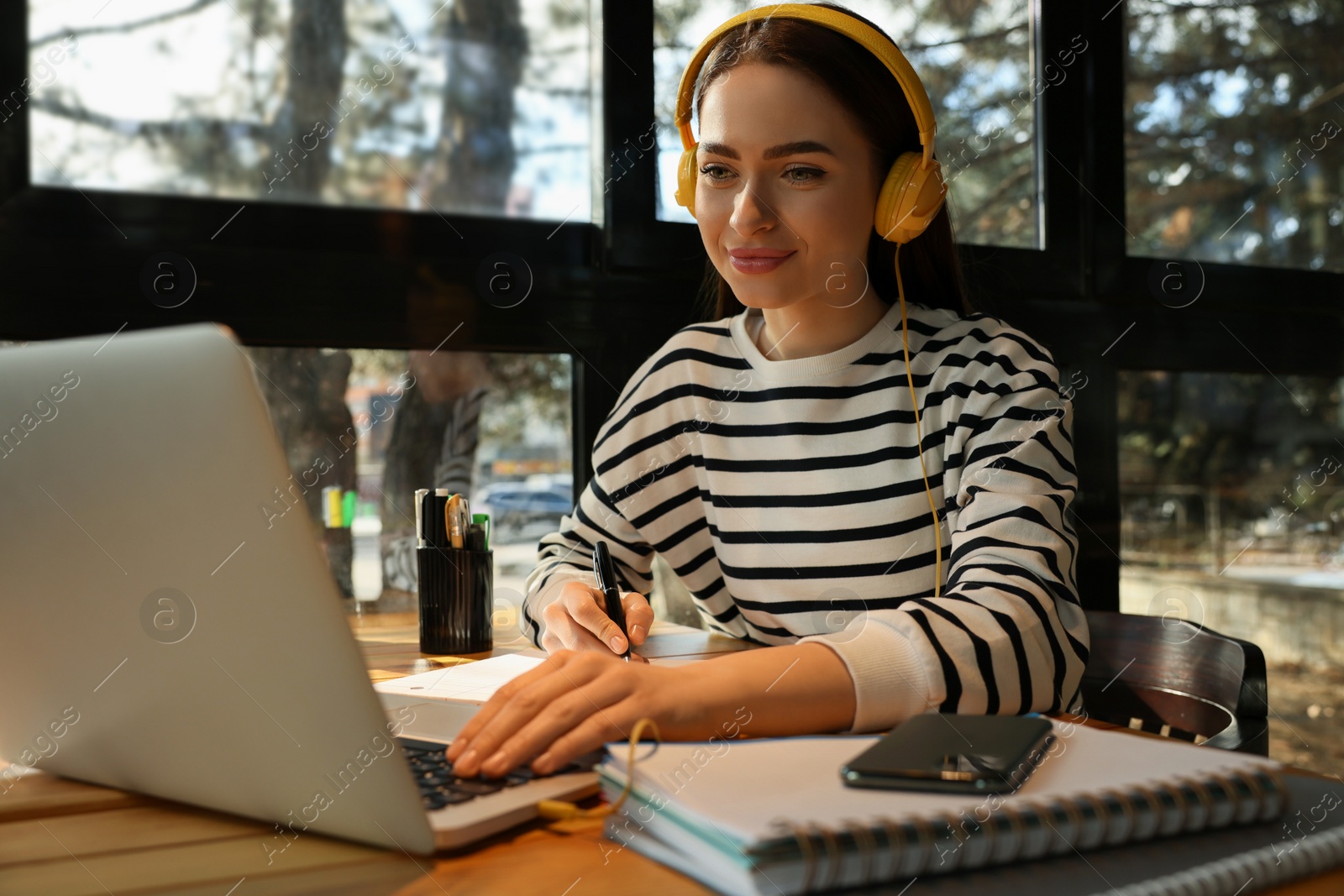 Photo of Young female student with laptop and headphones studying at table in cafe