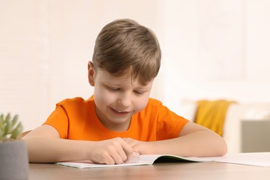 Little boy erasing mistake in his notebook at wooden desk indoors