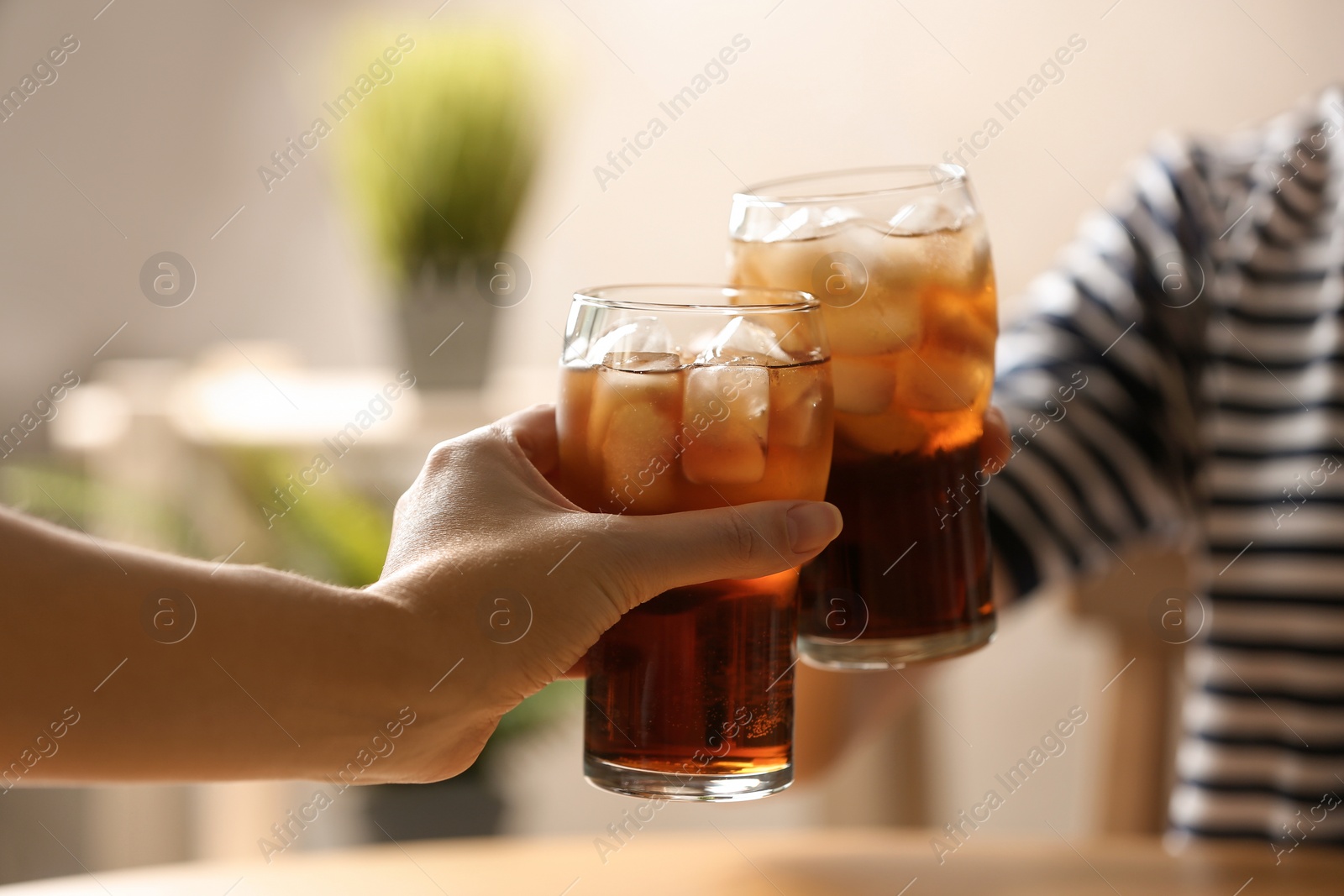 Photo of Women holding glasses of cola with ice at table, closeup