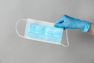 Photo of Doctor in medical gloves holding protective mask on light grey background, closeup