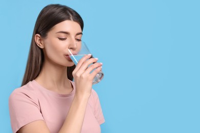 Photo of Healthy habit. Woman drinking fresh water from glass on light blue background. Space for text
