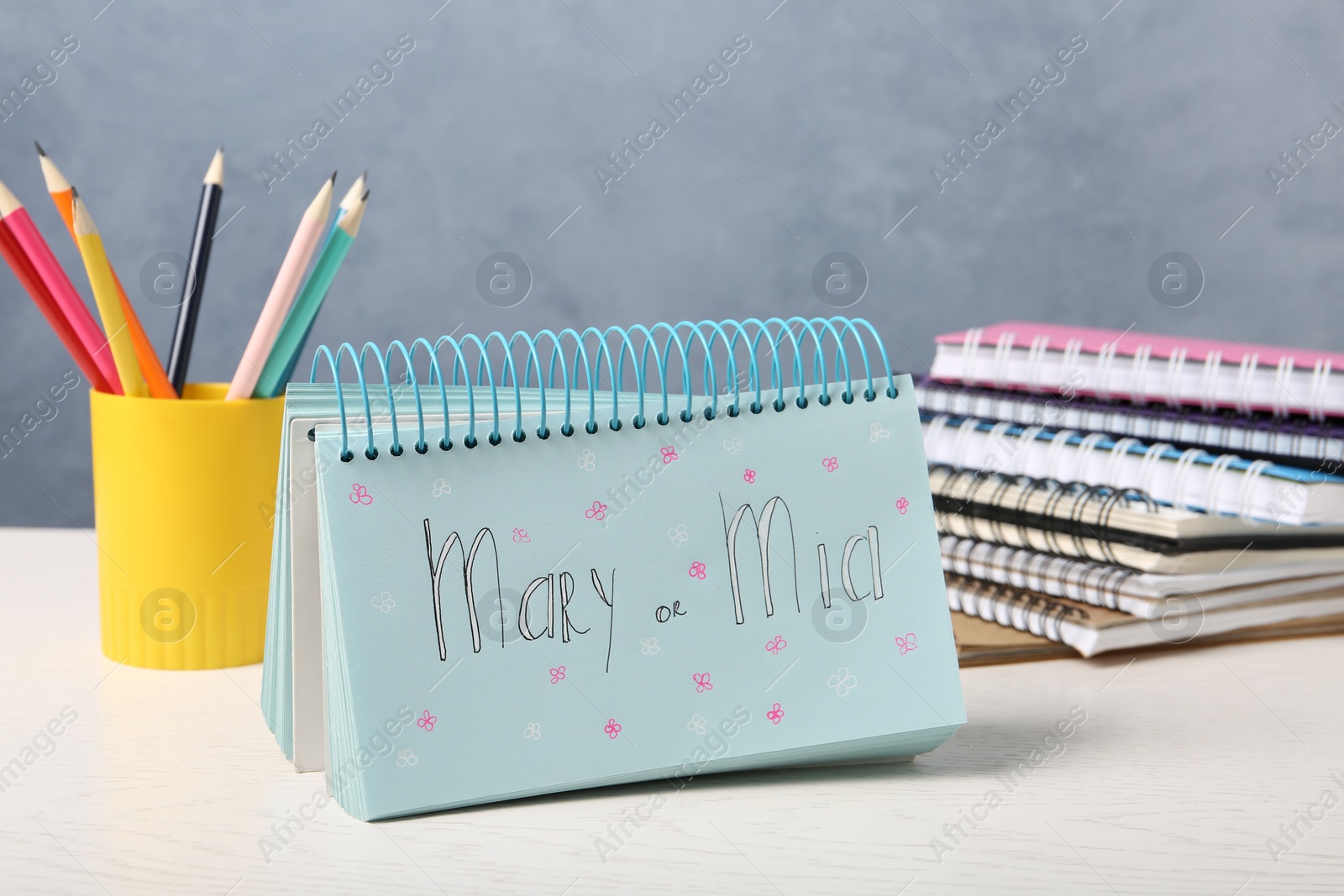 Photo of Notebook with written baby names and stationery on white wooden table