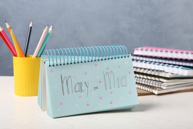 Notebook with written baby names and stationery on white wooden table