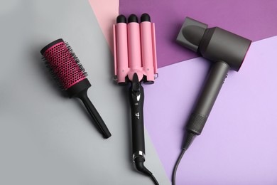 Hair dryer, brush and triple curling iron on color background, flat lay