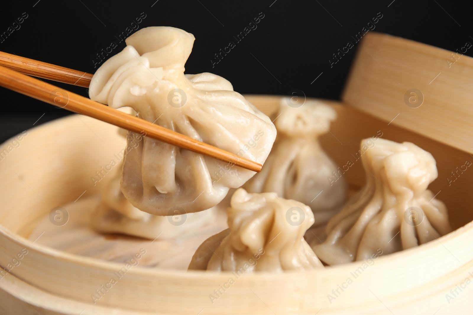 Photo of Chopsticks with baozi dumpling over bamboo steamer, closeup