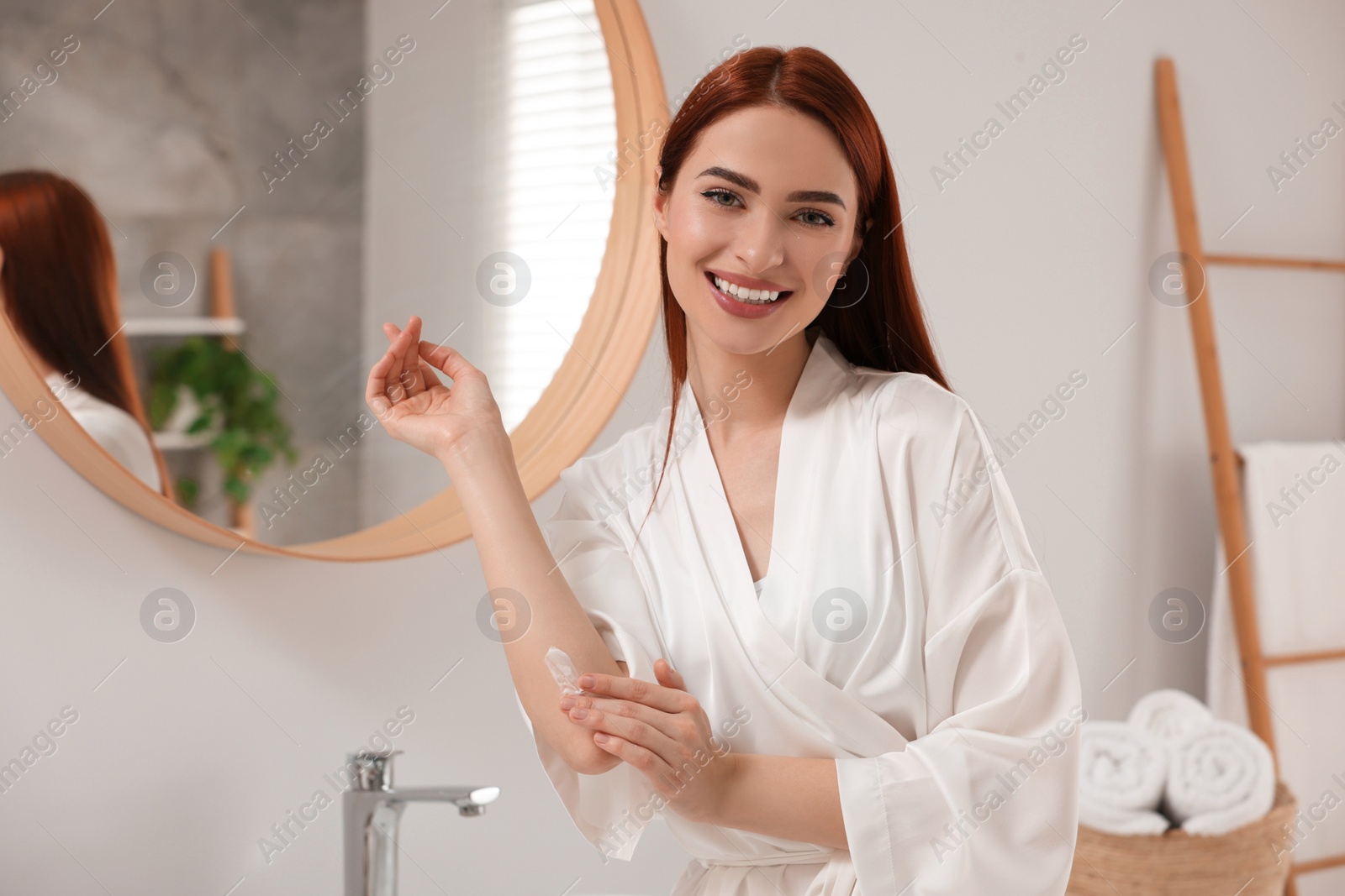 Photo of Beautiful young woman applying body cream onto elbow in bathroom, space for text