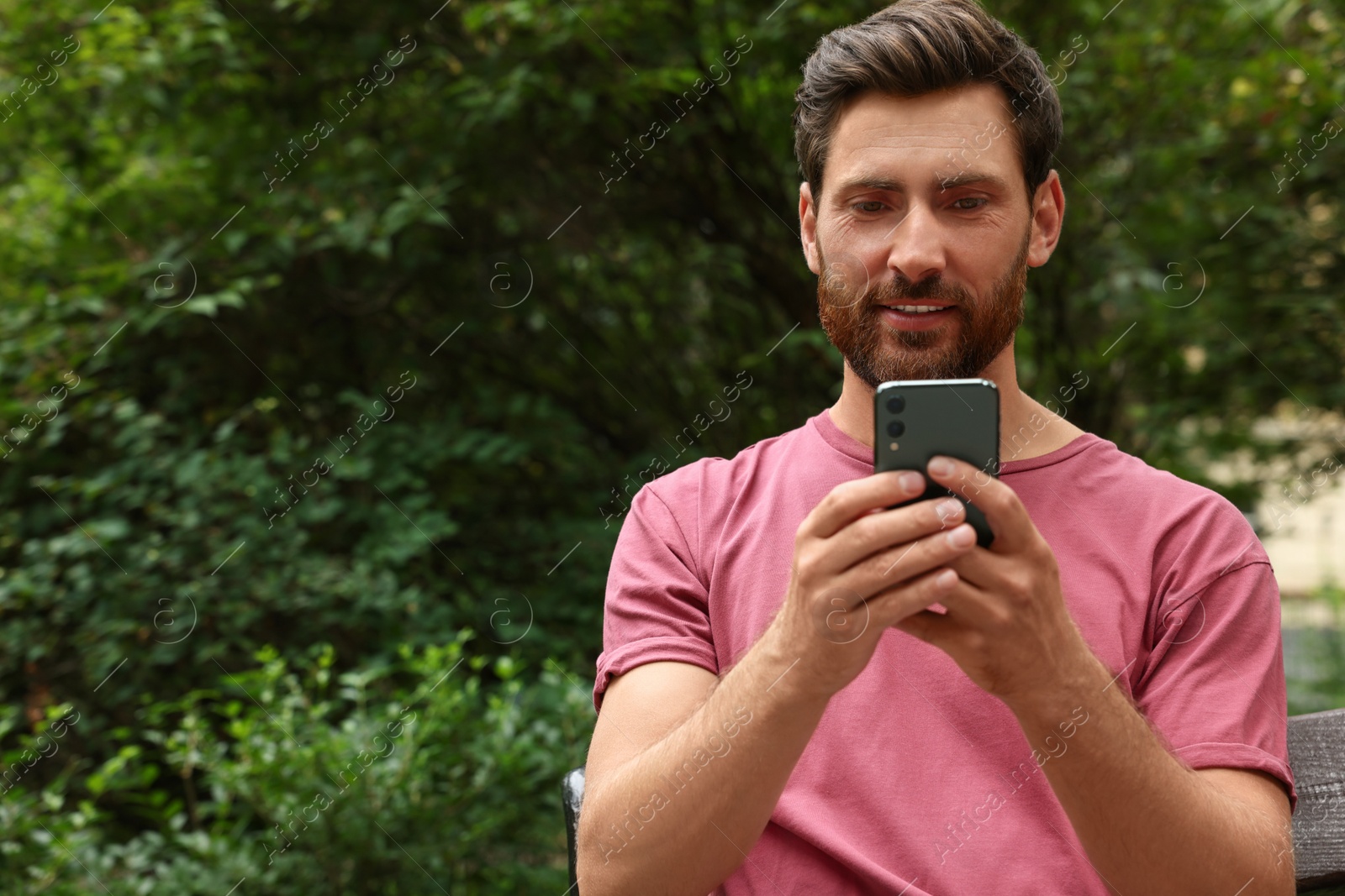 Photo of Handsome man using smartphone in park, space for text