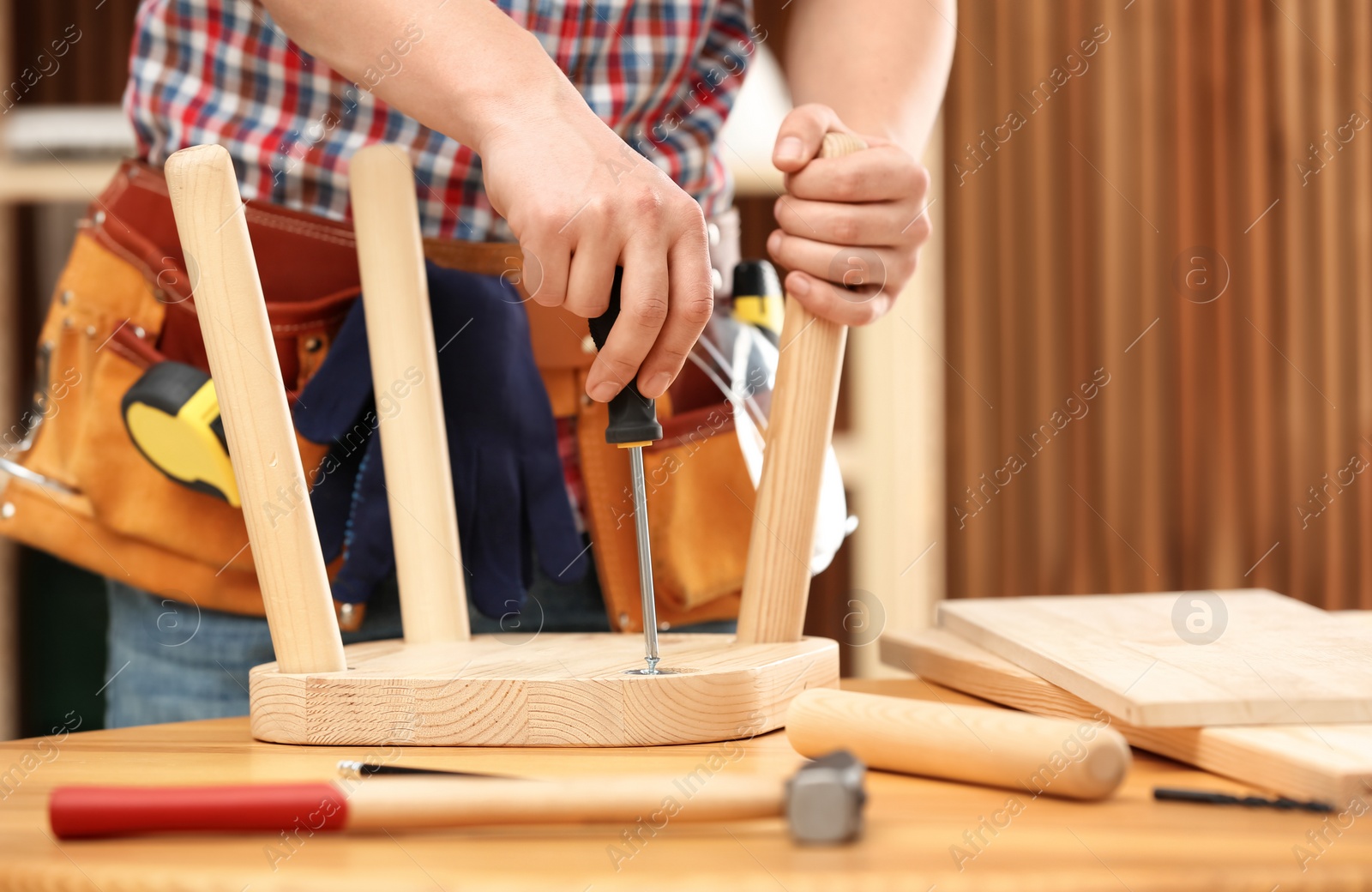 Photo of Young working man repairing wooden stool using screwdriver indoors, closeup