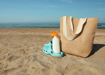 Bag, shoes and sun protection product on sandy beach. Space for text