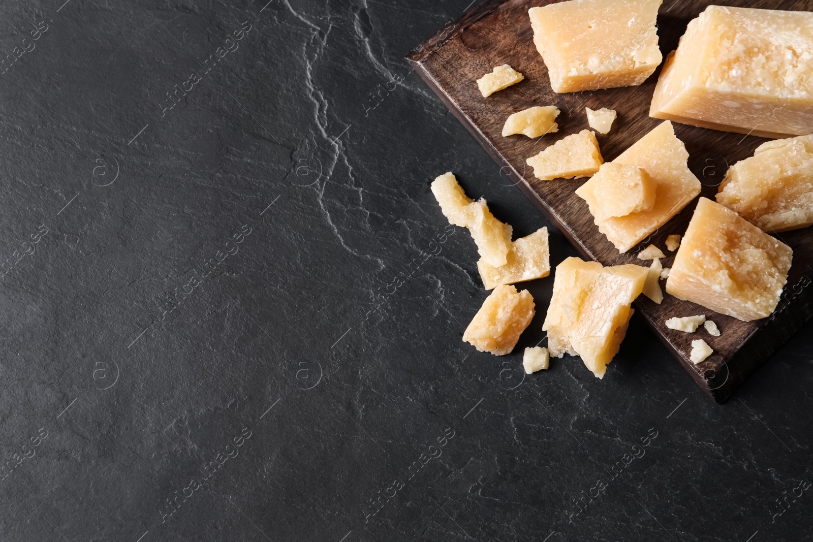 Photo of Pieces of delicious parmesan cheese on black table, top view. Space for text