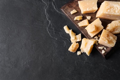 Photo of Pieces of delicious parmesan cheese on black table, top view. Space for text