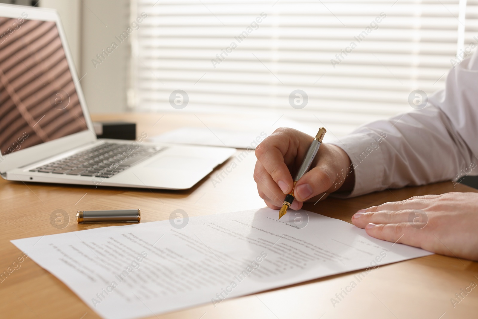 Photo of Notary signing document at wooden table in office, closeup