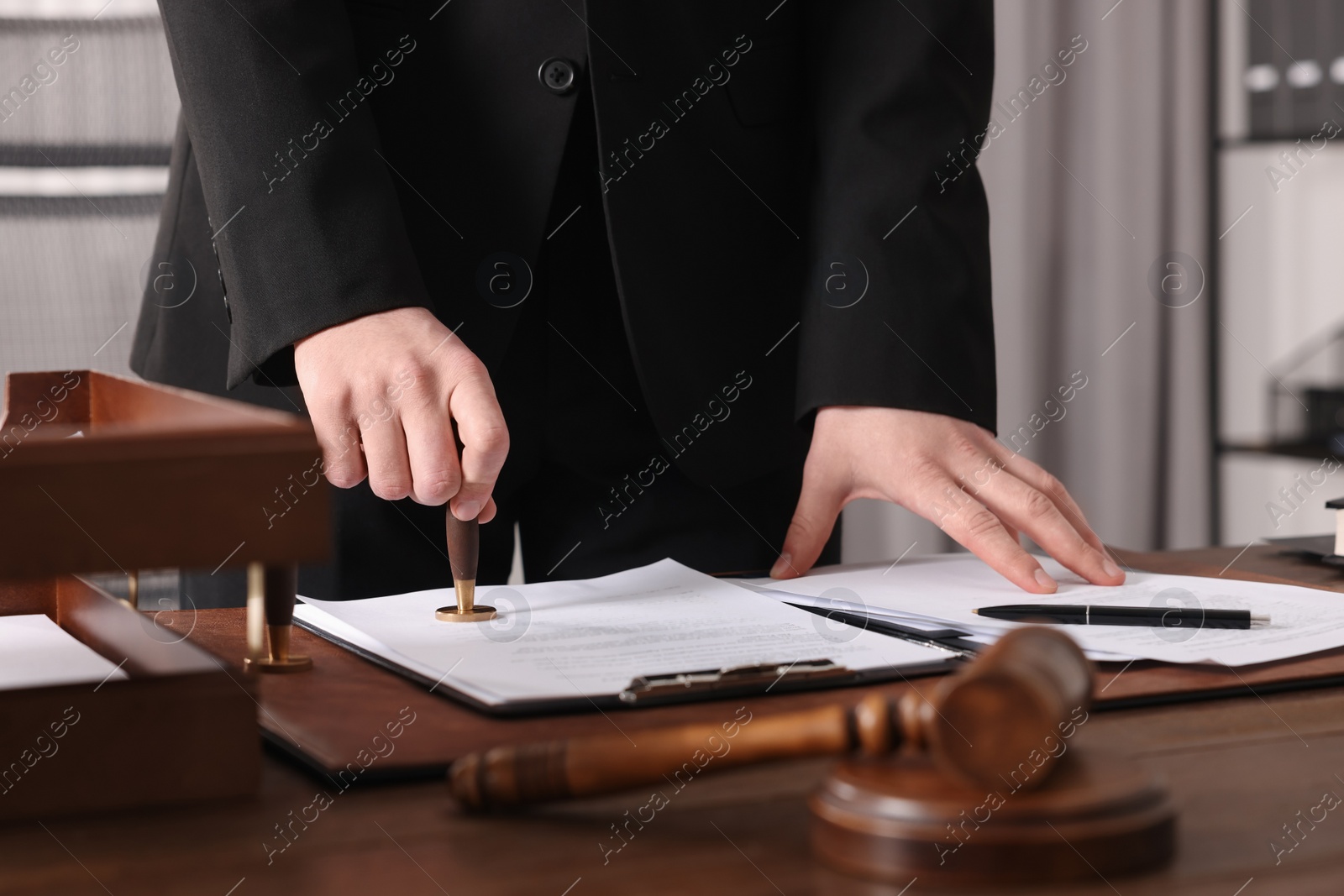 Photo of Notary stamping document at wooden table in office, closeup