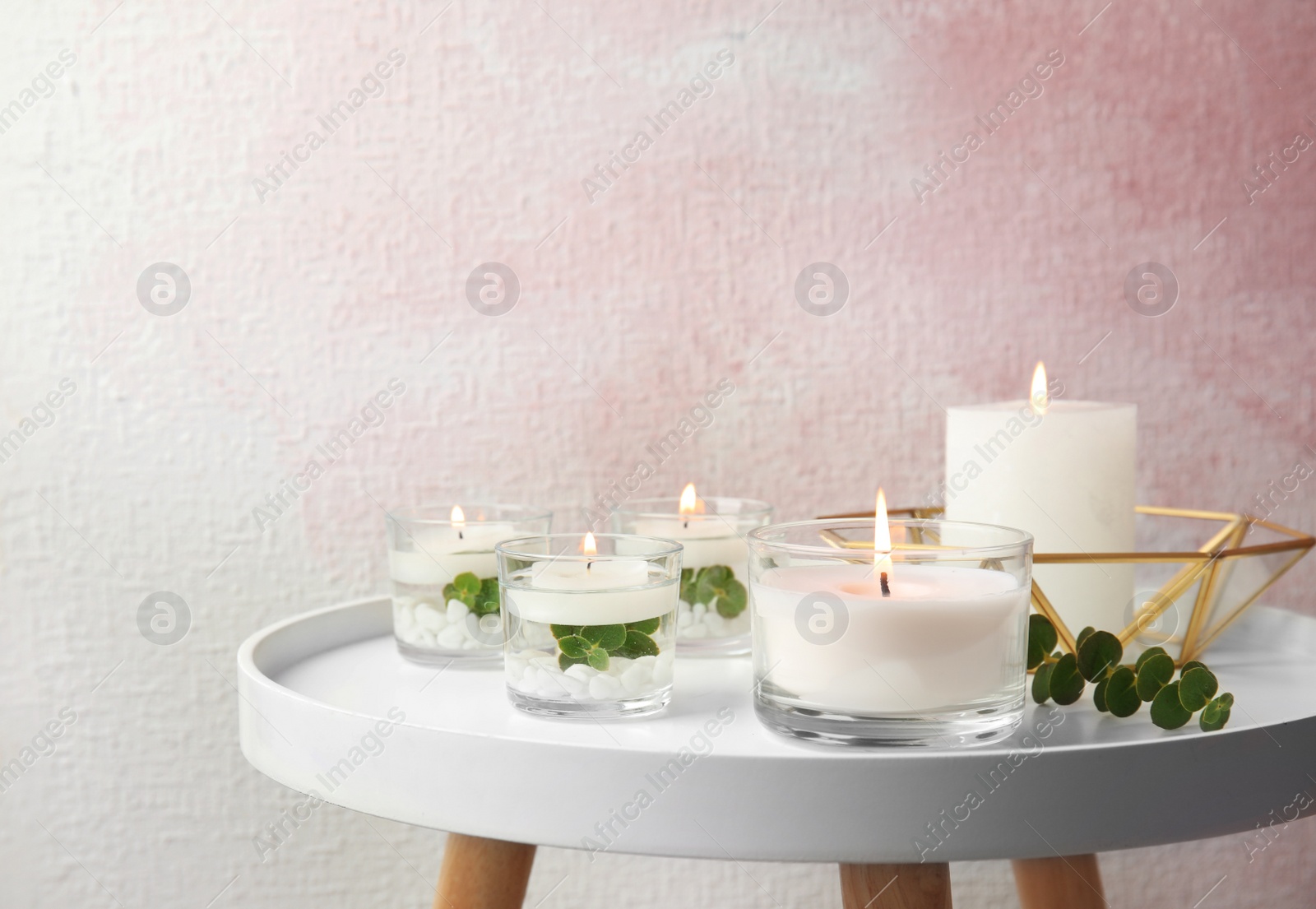 Photo of Composition with burning aromatic candles and eucalyptus on table near color wall. Space for text
