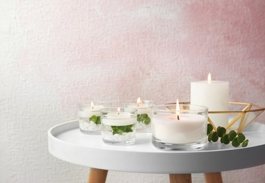 Composition with burning aromatic candles and eucalyptus on table near color wall. Space for text