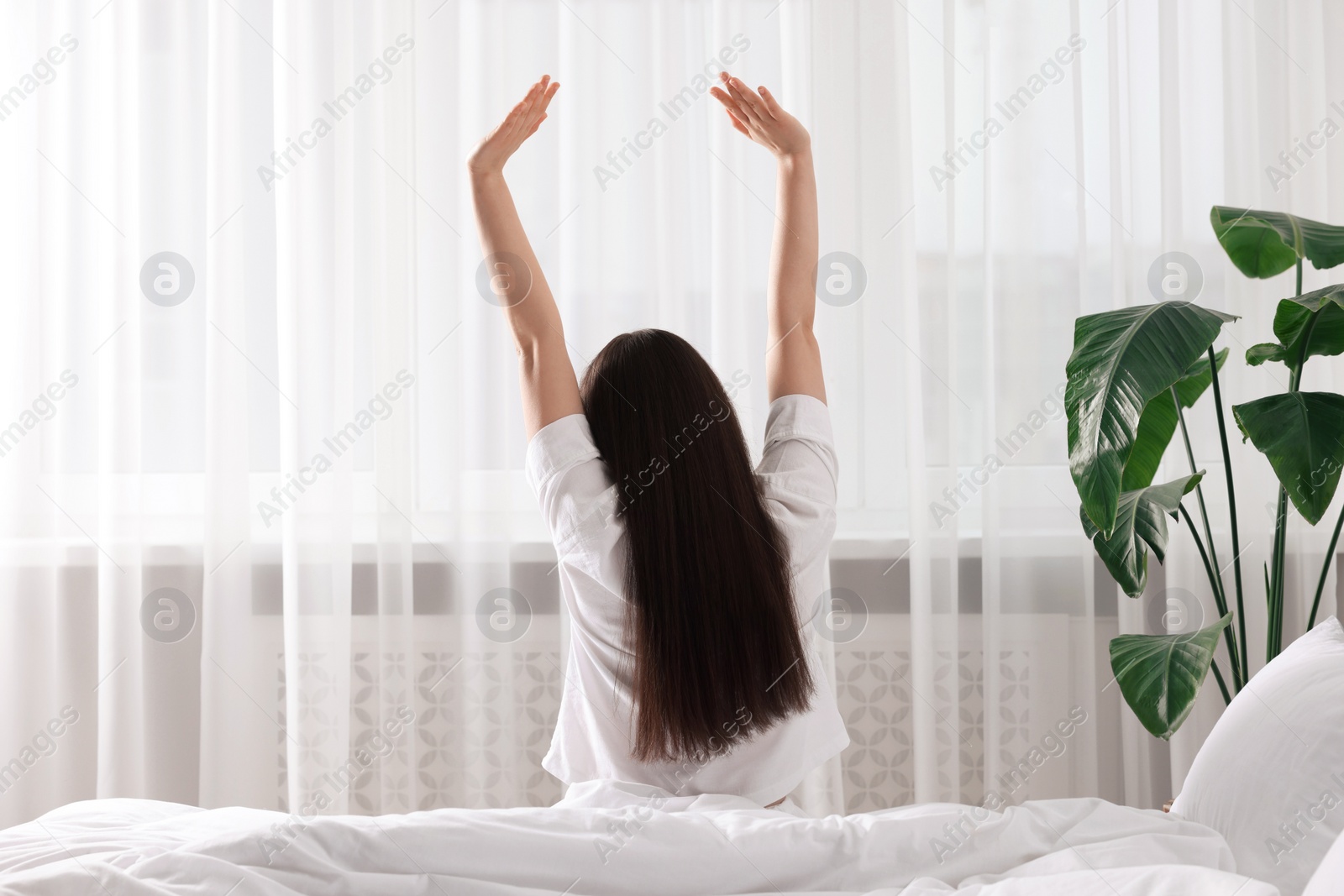 Photo of Woman stretching on bed at home, back view. Lazy morning