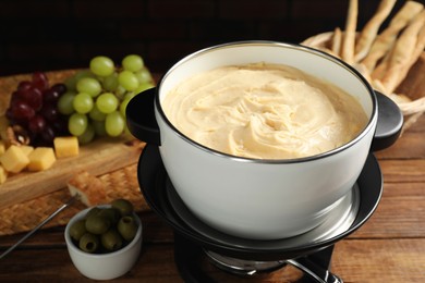 Photo of Fondue with tasty melted cheese, fork and different snacks on wooden table