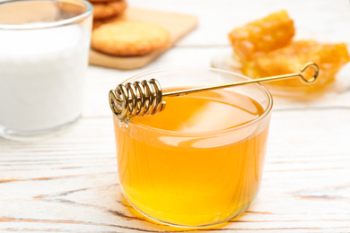 Photo of Tasty honey and metal dipper on white wooden table, closeup