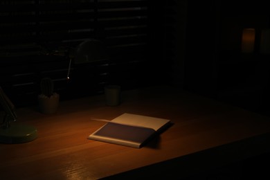Photo of Open book on wooden table at night