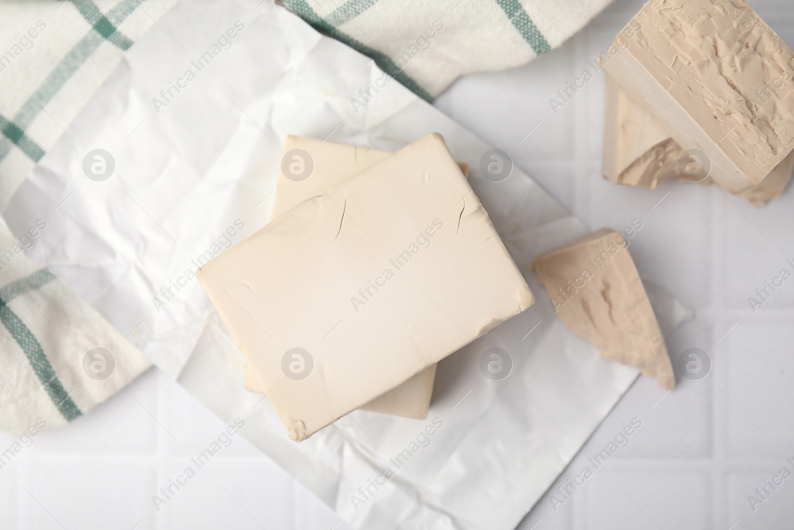 Photo of Blocks of compressed yeast on white tiled table, flat lay