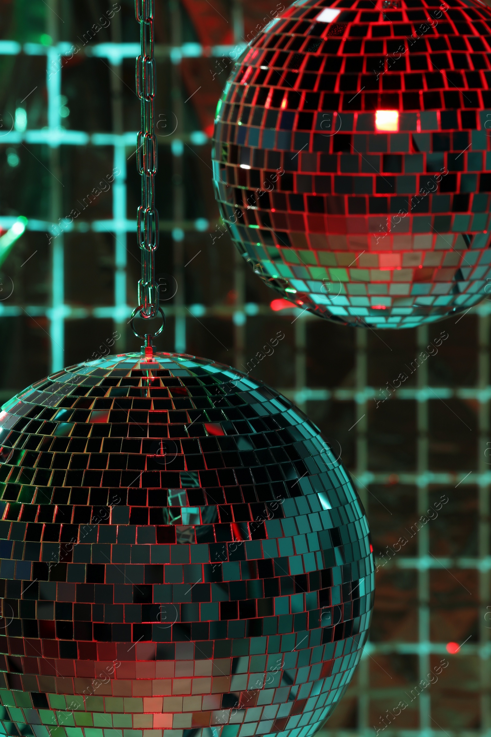 Photo of Shiny disco balls against foil party curtain under color lights