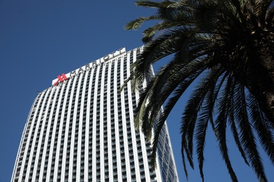 Batumi, Georgia - October 12, 2022: Mariott building and palm tree against blue sky, low angle view
