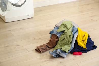 Pile of dirty laundry near washing machine indoors. Space for text