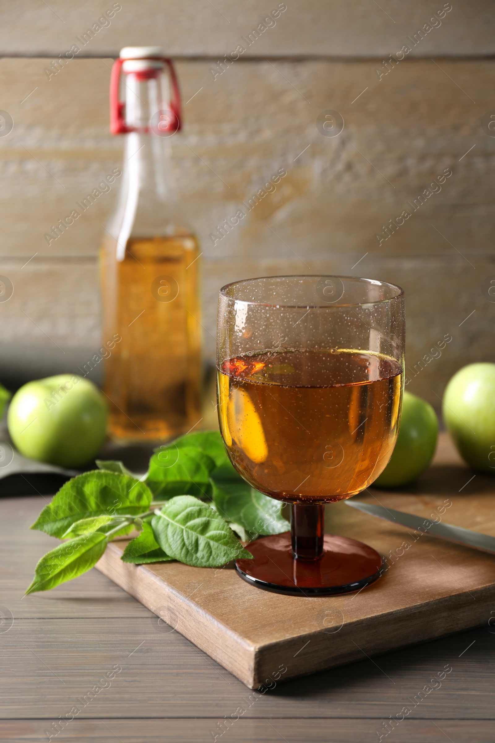 Photo of Delicious cider, apples and green leaves on wooden table, closeup
