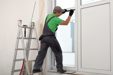 Worker in uniform installing double glazing window indoors