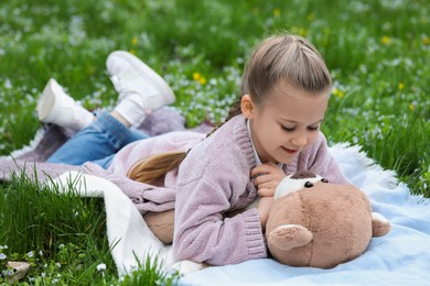 Photo of Little girl with teddy bear on plaid outdoors