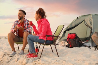 Photo of Couple with hot drinks on beach near camping tent